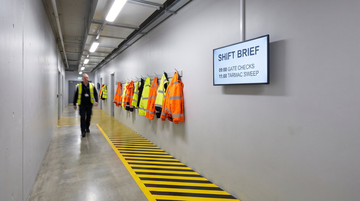 A screen in an airside staff corridor showing a shift brief