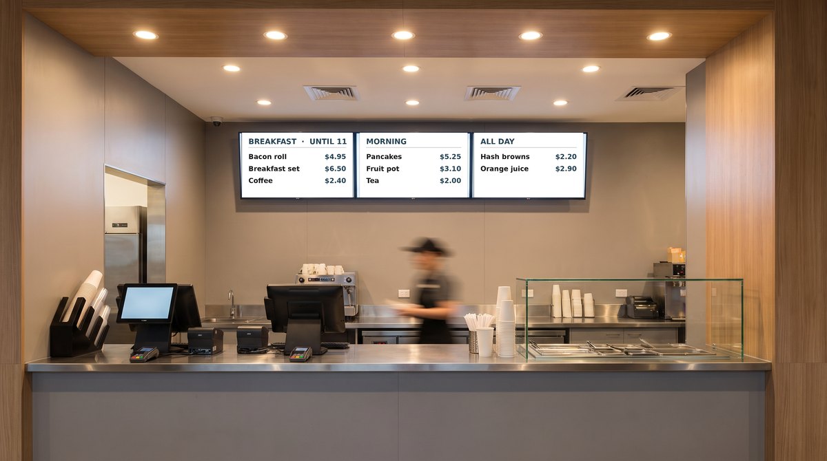 Three lit menu board screens above a quick service restaurant counter